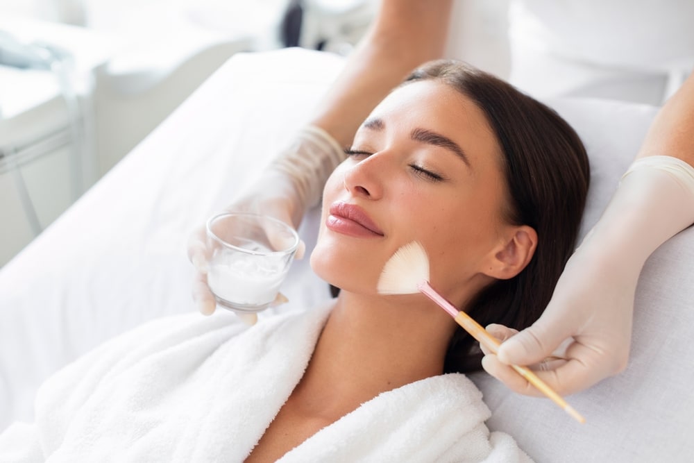 Cosmetologist cleaning face of a young woman before applying chemical peel